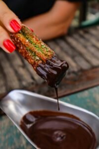 A Churro being dipped in Chocolate Sauce